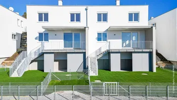 Moderne Reihenhäuser mit weißen Fassaden, großen Fenstern und Balkonen mit Blick ins Grüne.