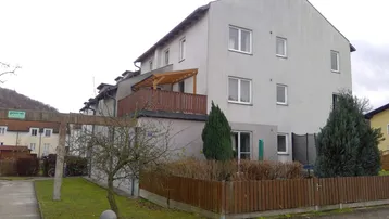 Mehrfamilienhaus mit heller Fassade, Balkon und kleinem Vorgartenbereich.