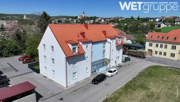 Mehrfamilienhaus mit rotem Ziegeldach und hellblauer Fassade in ländlicher Umgebung.
