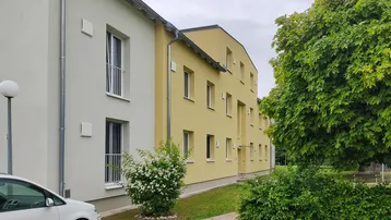 Moderne Mehrfamilienhäuser mit heller Fassade, großen Fenstern und gepflegten Grünflächen im Außenbereich.