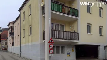 Mehrstöckiges Wohngebäude mit hellgelber Fassade, Balkonen und integrierter Tiefgarage an einer Straße.
