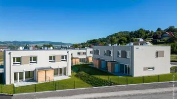 Moderne Reihenhäuser mit großen Fenstern und grüner Umgebung unter blauem Himmel.