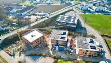 Luftaufnahme einer Baustelle mit mehreren im Bau befindlichen Gebäuden und Photovoltaikanlagen auf den Dächern.