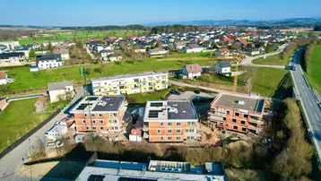 Luftaufnahme einer ländlichen Wohngegend mit Neubauten, grünen Feldern und Fernblick auf die Berge.
