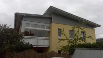 Modernes Gebäude mit gelber Fassade, Pultdach und verglastem Balkon.