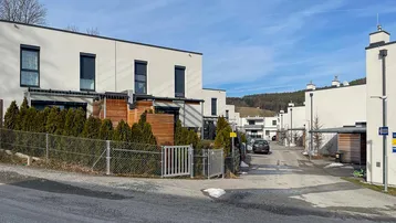 Moderne Reihenhäuser in einer Wohnsiedlung mit gepflegten Vorgärten und Carports unter blauem Himmel.