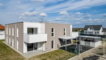 Modernes Mehrfamilienhaus mit Balkonen, Terrassen und Carport in ländlicher Umgebung.