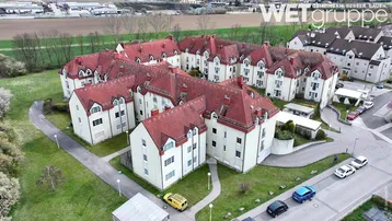 Luftaufnahme eines Wohnkomplexes mit mehreren Gebäuden und roten Dächern, umgeben von Grünflächen.