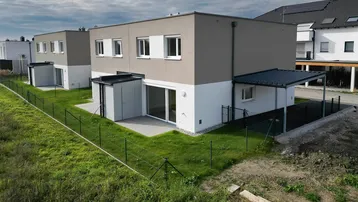 Moderne Reihenhäuser mit schlichtem Design, kleinen Gärten und überdachten Stellplätzen in Neubaugebiet.