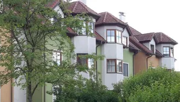 Reihenhäuser mit farbigen Fassaden, Erkern und Ziegeldächern, umgeben von üppigem Grün.