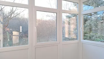 Verglaster Wintergarten mit vielen Fenstern und Blick ins Grüne, ideal zum Entspannen und Genießen.