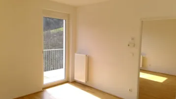 Lichtdurchfluteter Raum mit Holzboden, Heizkörper und französischem Balkon.