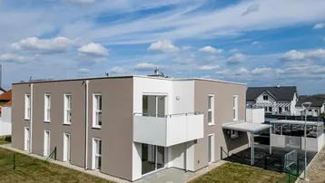 Modernes Neubau-Mehrfamilienhaus mit klarer Architektur, Balkon, Terrasse und Carport.