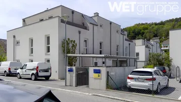 Modernes Mehrfamilienhaus mit weißer Fassade, Carport und Grünblick auf die umliegende Hügellandschaft.