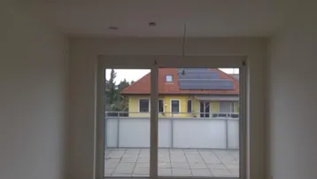 Innenraum mit großem Fenster und Blick auf eine geflieste Terrasse und ein Nachbarhaus.
