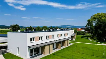 Vogelperspektive auf moderne Reihenhäuser mit Photovoltaikanlagen auf den Flachdächern und weitem Blick in die Landschaft.