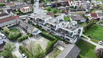 Luftaufnahme eines modernen Wohnkomplexes mit Flachdächern, Balkonen und Spielplatz in ländlicher Umgebung.
