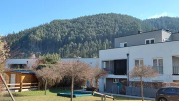 Moderne Wohnanlage mit Spielplatz und Blick auf bewaldete Berge unter blauem Himmel.