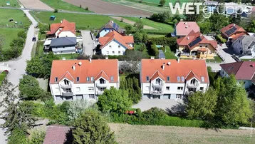 Luftaufnahme von zwei modernen Mehrfamilienhäusern mit roten Dächern in einer grünen, ländlichen Umgebung.