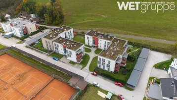Luftaufnahme einer modernen Wohnanlage mit mehreren Gebäuden, Gründächern, Carports und angrenzenden Tennisplätzen.