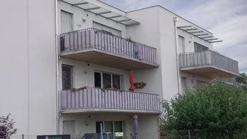 Moderne Wohnhausfassade mit mehreren Balkonen, Glasüberdachungen und Rollläden an den Fenstern.