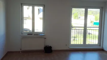 Heller Wohnraum mit Laminatboden, großem Fenster und Zugang zu einem französischen Balkon.