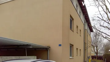 Gebäudefassade eines Mehrfamilienhauses mit beige gestrichener Wand und Carport.