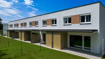 Moderne Reihenhäuser mit Flachdach, großen Fenstern und grüner Rasenfläche.
