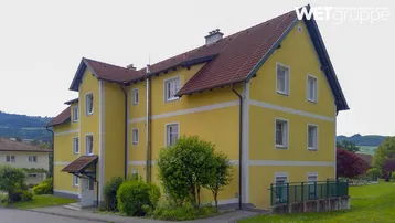 Gut erhaltenes Gebäude mit gelber Fassade, Satteldach und Blick ins Grüne.