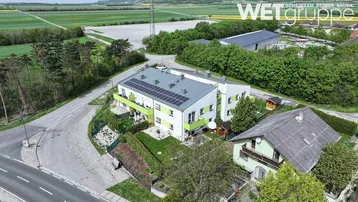 Luftaufnahme eines modernen Wohngebäudes mit Solaranlage und grüner Umgebung.
