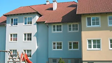 Mehrfamilienhaus mit hellen Fassaden, roten Ziegeldächern und einem kleinen Spielplatz im Vorgarten.