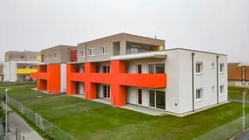 Moderne Wohnanlage mit mehreren Einheiten, farbigen Akzenten und privaten Gartenbereichen.