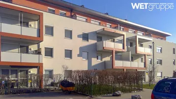 Modernes Mehrfamilienhaus mit mehreren Balkonen und gepflegter Außenanlage unter blauem Himmel.