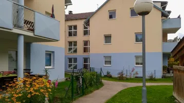 Wohngebäude mit beigefarbener und hellblauer Fassade, umgeben von einem gepflegten Gartenbereich.