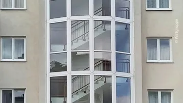 Mehrstöckiges Wohngebäude mit markantem verglastem Treppenhaus und Balkonen an den Seiten.