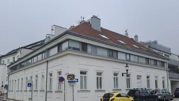 Weißes Eckgebäude mit klassischer Architektur und modernen Dachfenstern an einer Stadtstraße.