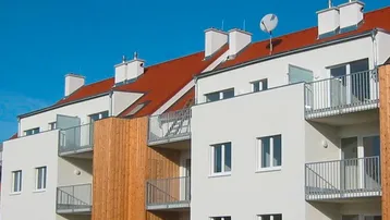 Moderne Wohnanlage mit weißer Fassade, roten Ziegeldächern und Balkonen mit Holzverkleidung.