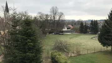 Weitläufiger Blick über einen großen Garten mit Bäumen und einer Kirche im Hintergrund.