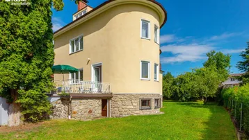 Gelbe Fassade eines Hauses mit kleinem Balkon und gepflegtem Rasenbereich.