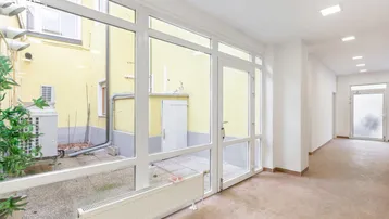 Heller Flur mit großen Fenstern, die einen Blick auf den Innenhof und die Klimaanlage bieten.