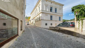 Historisches Gebäude an einer gepflasterten Gasse mit traditioneller Architektur und einem Weinladen im Vordergrund.