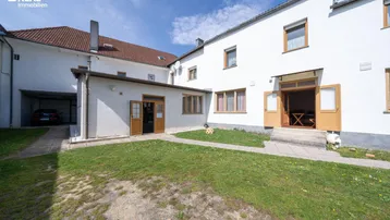 Außenansicht des Gebäudes mit weißer Fassade, kleinem Rasenbereich und Carport.