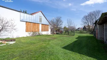 Weitläufiger Rasenbereich neben einem Gebäude mit Holzverkleidung und Blick in die Ferne.