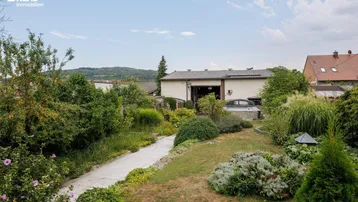 Gepflegter Gartenbereich mit einem Weg, üppiger Vegetation und einem Whirlpool im Hintergrund.
