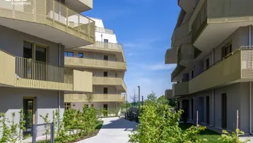 Moderne Wohngebäude mit Balkonen und begrünten Außenanlagen unter blauem Himmel.
