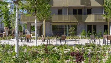 Moderne Wohngebäude umgeben von gepflegten Grünflächen und Sitzgelegenheiten im Freien.