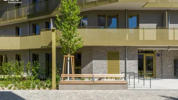 Moderne Wohnanlage mit Sitzbänken und junger Bepflanzung im Außenbereich.