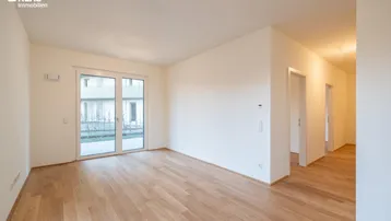 Helles, leeres Zimmer mit Holzboden und Zugang zu einem privaten Gartenbereich.
