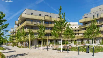 Moderne Wohnanlage mit mehreren Gebäuden, begrüntem Innenhof und Sitzbänken unter blauem Himmel.