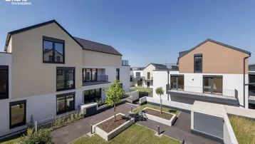 Moderne Reihenhäuser mit gepflegten Außenanlagen und klarem Design unter blauem Himmel.